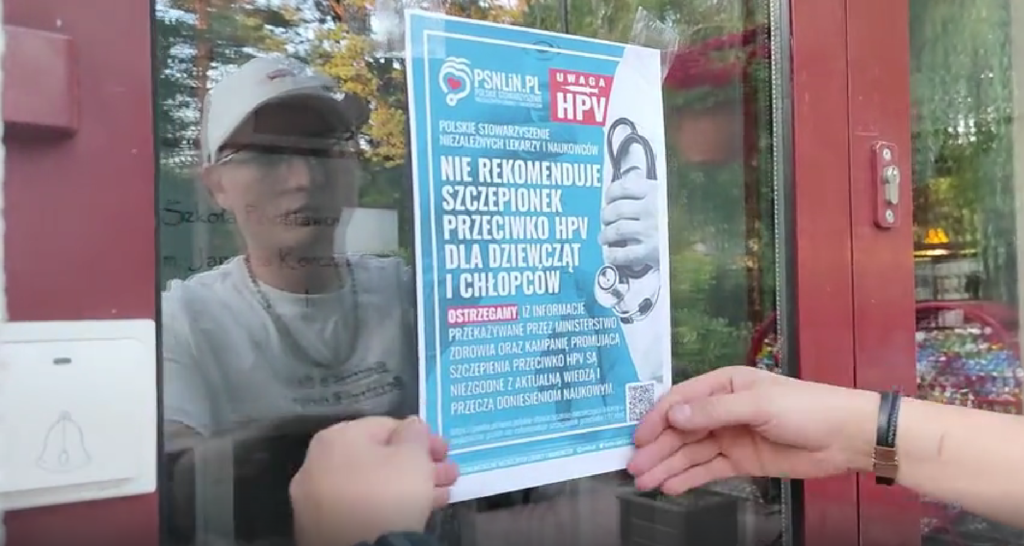 Rafał Kędzierski wieszający plakat PSNLiN na drzwiach wejściowych szkoły podstawowej